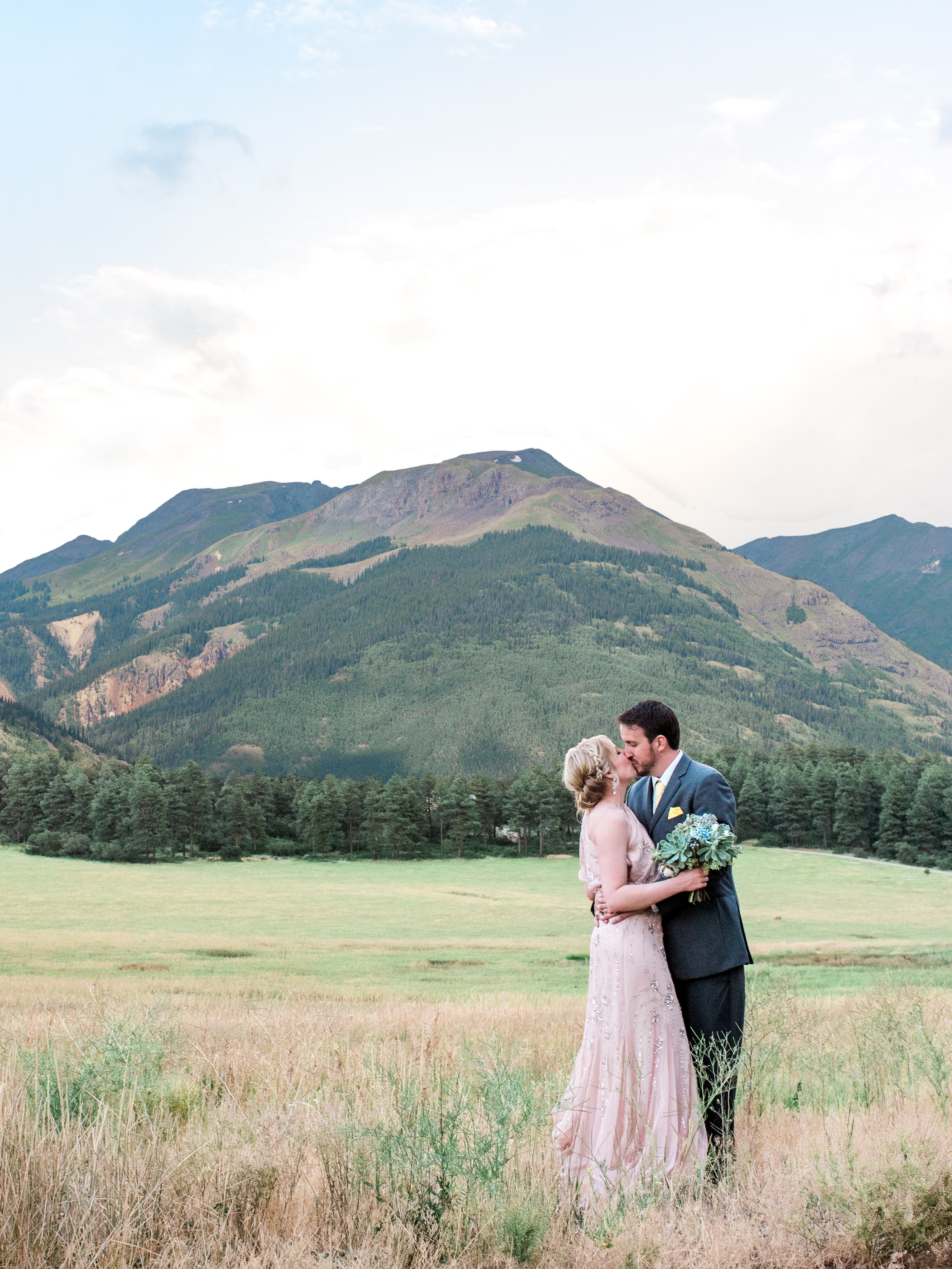 Colorado Destination Wedding couple standing in a field at the base of a mountain embracing and kissing by Wedding Photographer in Houston Thomas Ross Photography